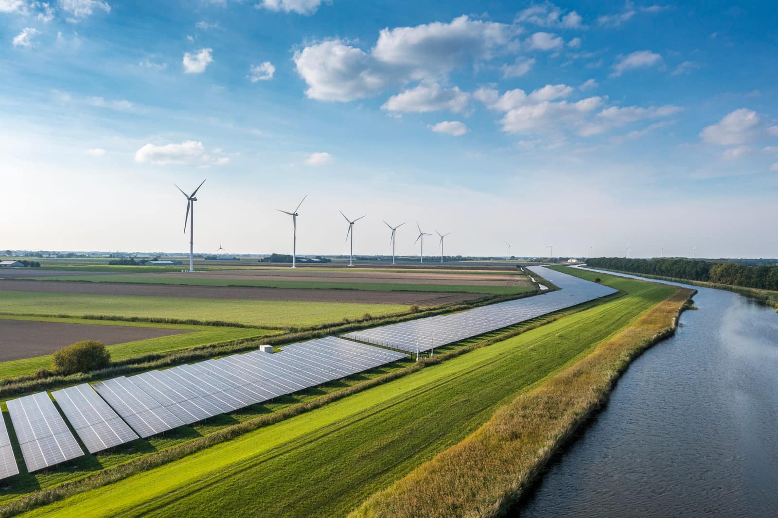 Wind turbines and solar panels alongside agricultural fields and a canal