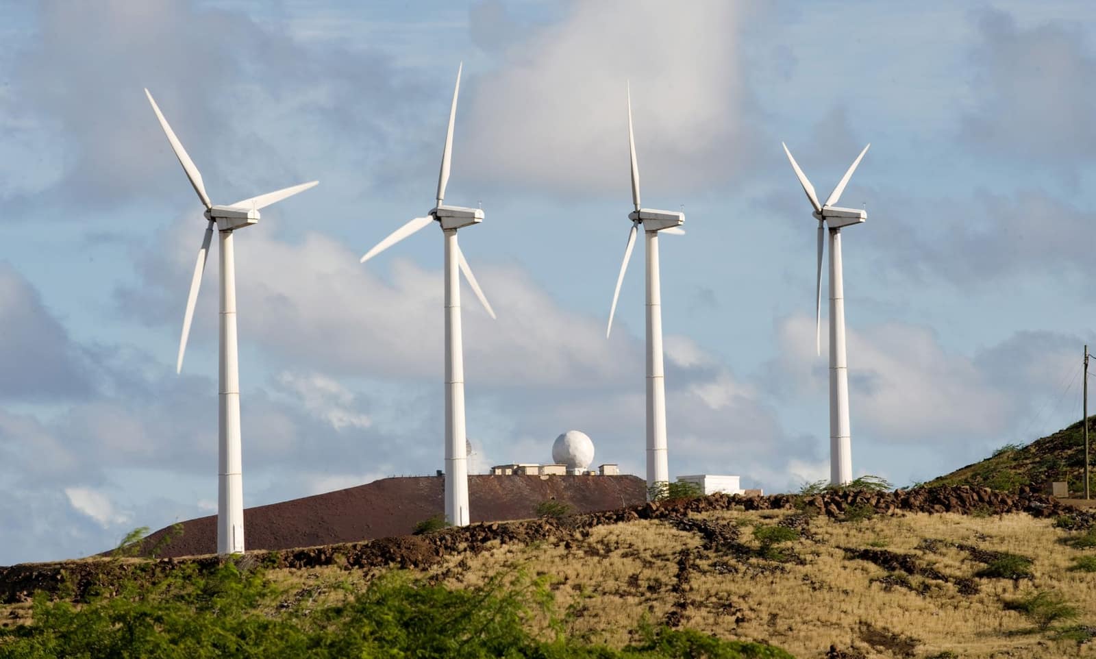 Wind turbines on a green hill under an open sky