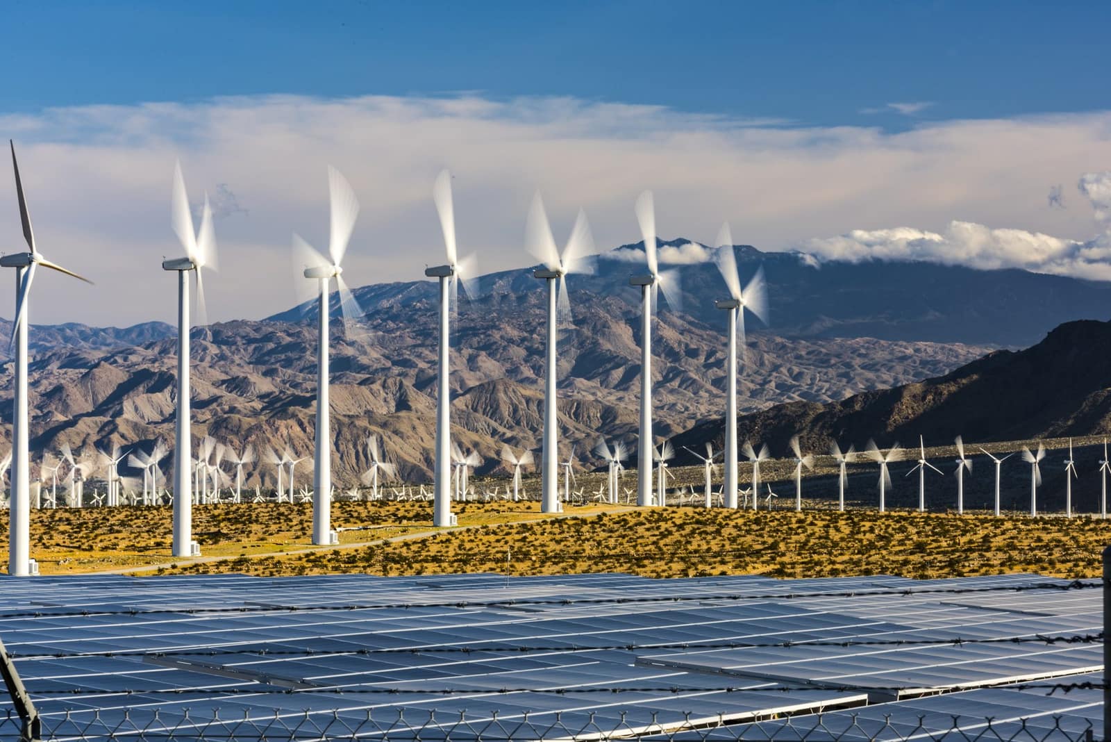 Wind turbines and a solar array against a mountain backdrop