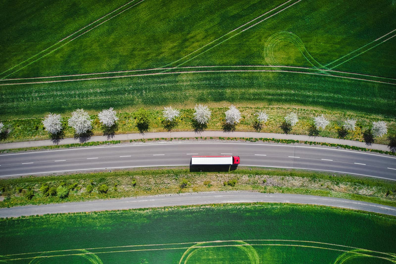 Aerial view of a truck on a road through green agricultural fields